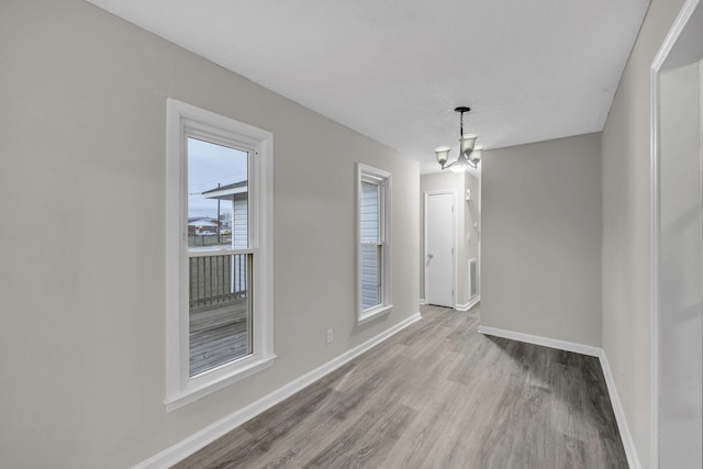 unfurnished dining area with wood finished floors, baseboards, and a notable chandelier