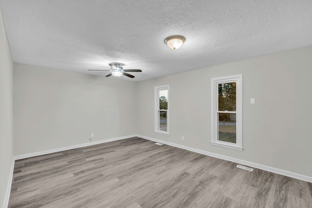 empty room featuring a textured ceiling, baseboards, visible vents, a ceiling fan, and wood finished floors