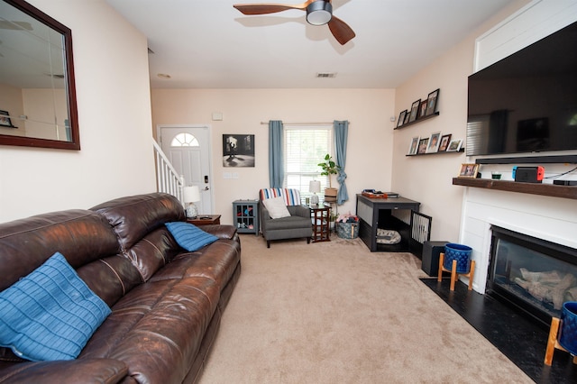 carpeted living room with a fireplace with flush hearth, a ceiling fan, visible vents, and stairway