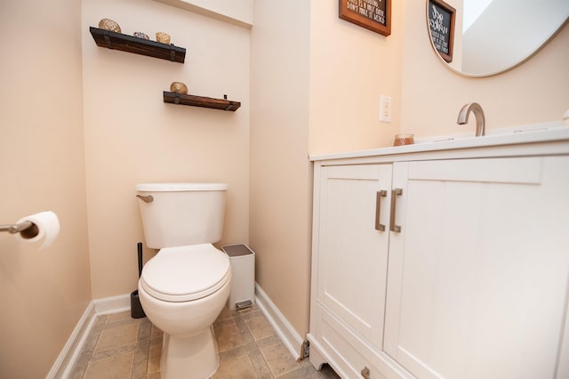 half bath featuring stone finish flooring, baseboards, toilet, and vanity