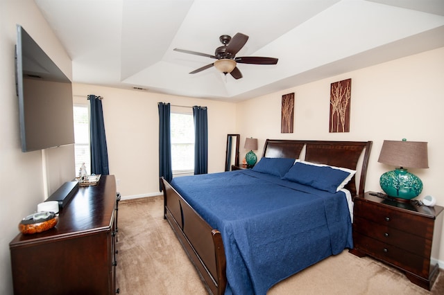 bedroom with a ceiling fan, a tray ceiling, light colored carpet, baseboards, and visible vents