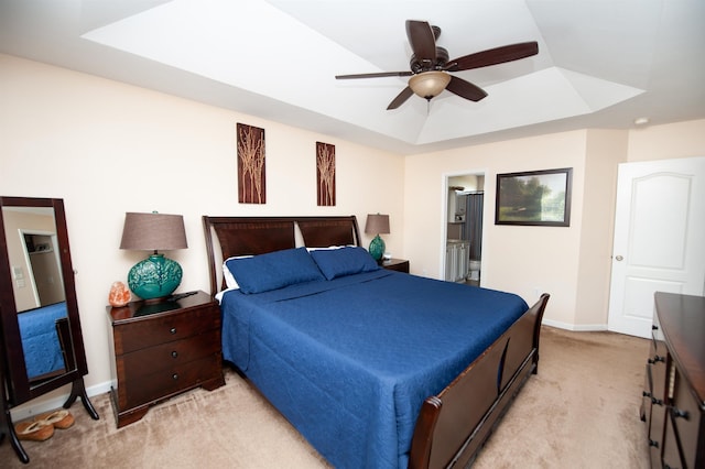 bedroom with a tray ceiling, ensuite bath, baseboards, light colored carpet, and ceiling fan