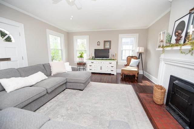 living area with wood finished floors, ornamental molding, baseboards, a brick fireplace, and ceiling fan