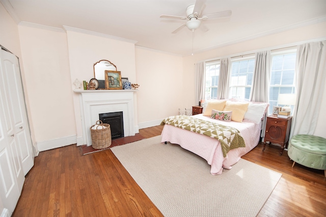 bedroom featuring a fireplace with flush hearth, baseboards, wood finished floors, and ornamental molding
