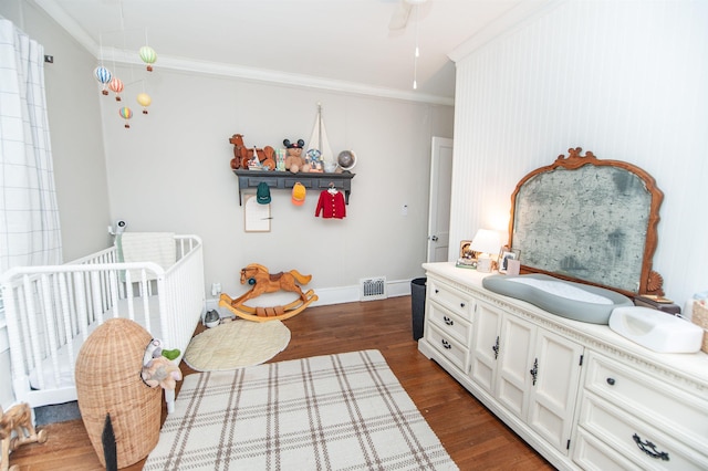 bedroom with visible vents, a crib, dark wood-style floors, and crown molding
