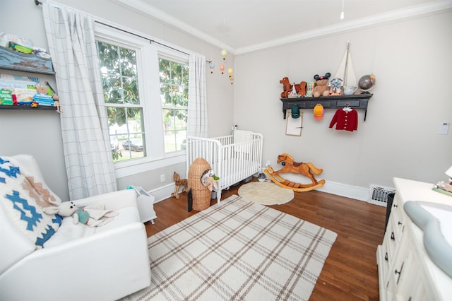 bedroom with a nursery area, wood finished floors, baseboards, ornamental molding, and visible vents