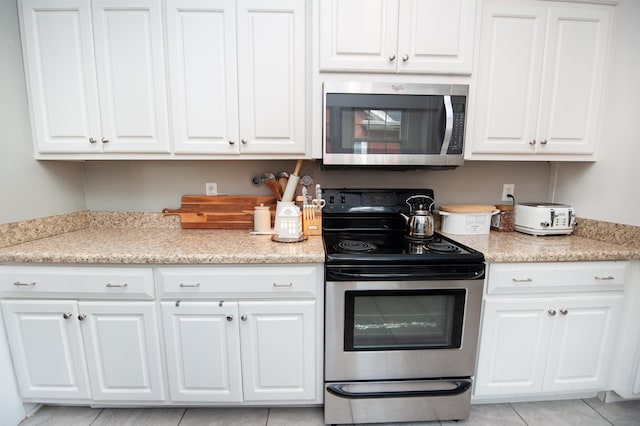 kitchen featuring white cabinetry, light stone countertops, stainless steel appliances, and light tile patterned flooring