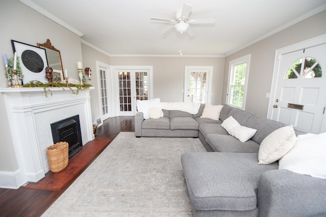 living room with crown molding, a ceiling fan, a brick fireplace, and wood finished floors