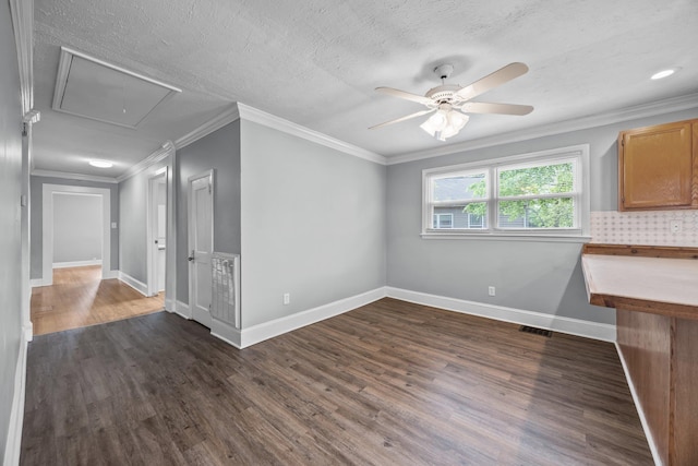 unfurnished living room featuring attic access, dark wood-style flooring, baseboards, ceiling fan, and ornamental molding