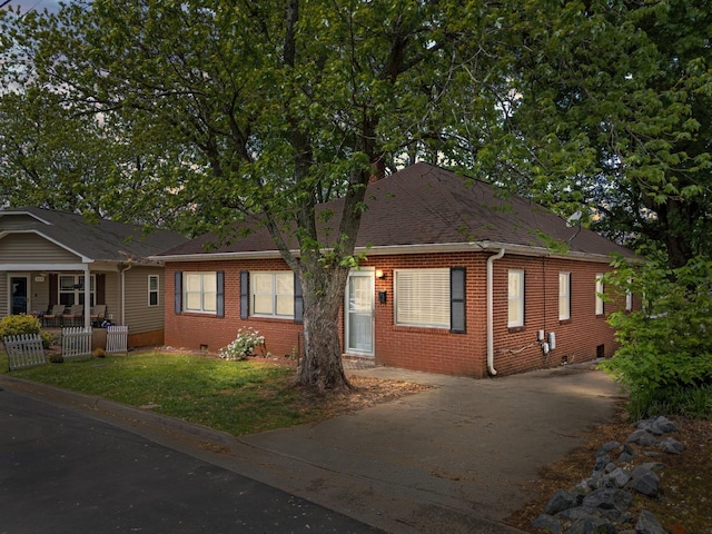 view of front facade featuring concrete driveway, a front lawn, fence, brick siding, and roof with shingles