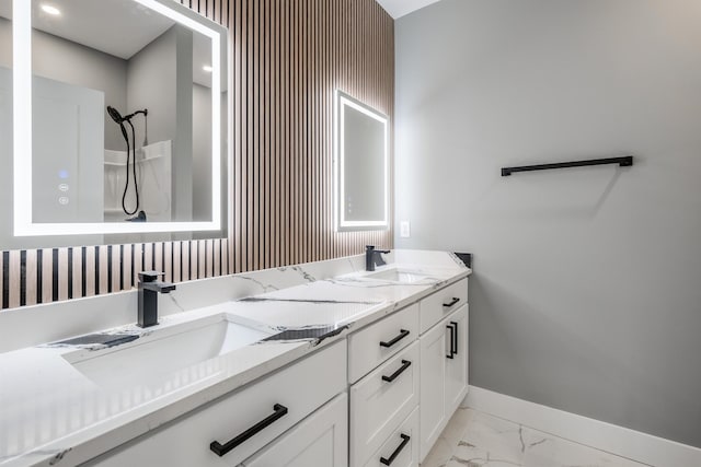 full bath featuring double vanity, marble finish floor, baseboards, and a sink
