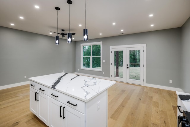 kitchen with a kitchen island, light wood-type flooring, light stone countertops, and baseboards