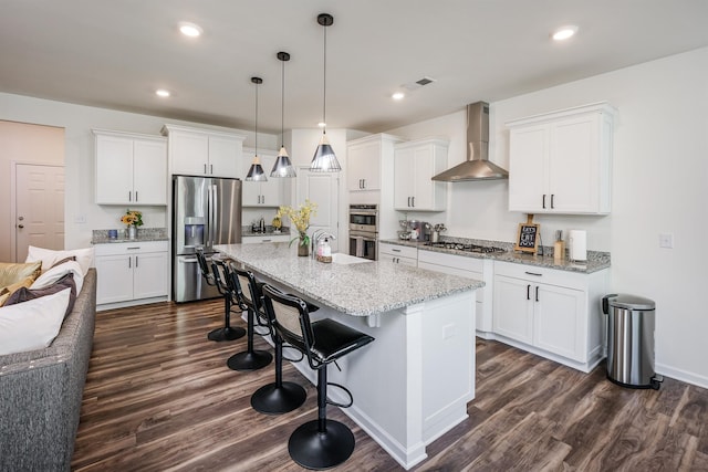 kitchen with appliances with stainless steel finishes, wall chimney range hood, dark wood-style floors, visible vents, and a kitchen breakfast bar