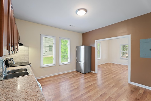 kitchen with a sink, electric panel, light countertops, freestanding refrigerator, and plenty of natural light