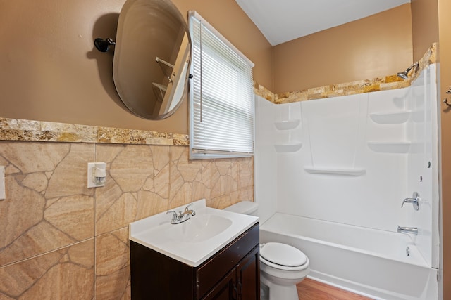 bathroom featuring tile walls, a wainscoted wall, toilet, shower / washtub combination, and vanity