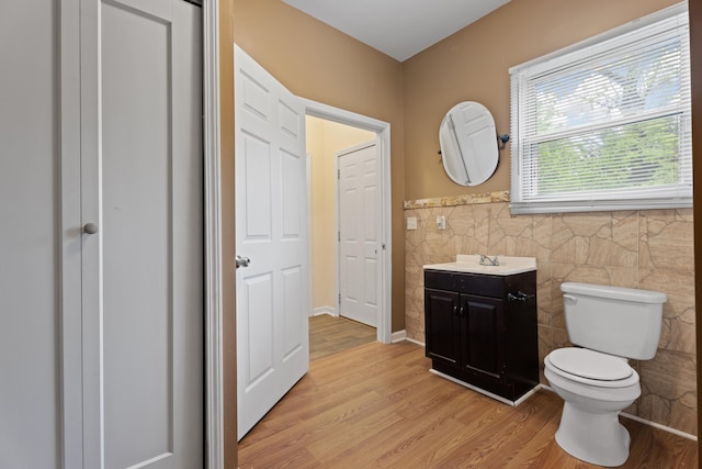 bathroom featuring a wainscoted wall, toilet, tile walls, wood finished floors, and vanity