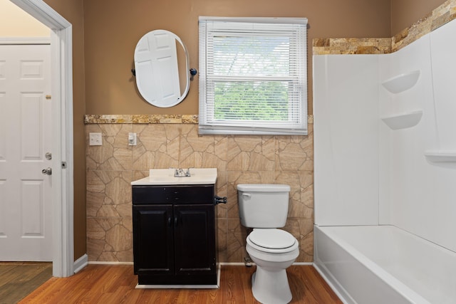 full bathroom featuring wood finished floors, toilet, wainscoting, and tile walls