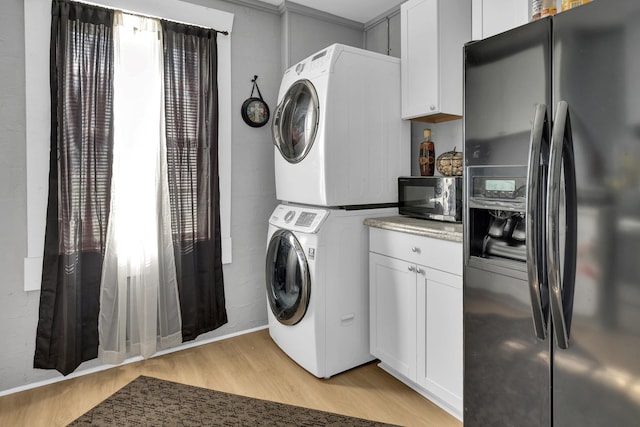 washroom with stacked washing maching and dryer, light wood-type flooring, laundry area, and baseboards