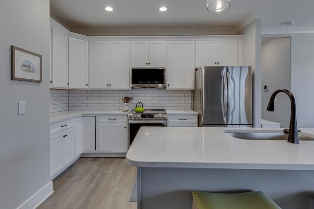 kitchen with decorative backsplash, light wood-style floors, appliances with stainless steel finishes, white cabinets, and a sink