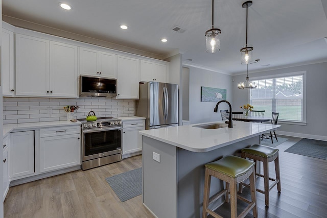 kitchen featuring light wood finished floors, a sink, tasteful backsplash, crown molding, and appliances with stainless steel finishes