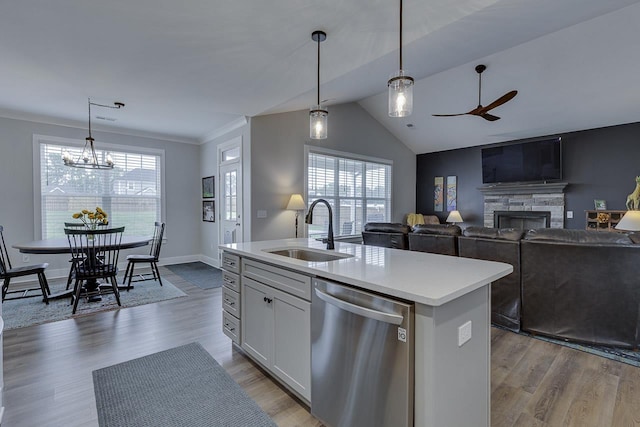 kitchen with a sink, a ceiling fan, a stone fireplace, light countertops, and stainless steel dishwasher