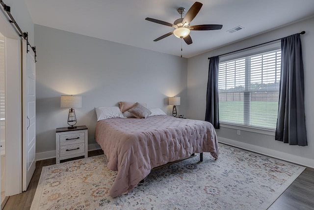 bedroom featuring wood finished floors, visible vents, baseboards, and a barn door