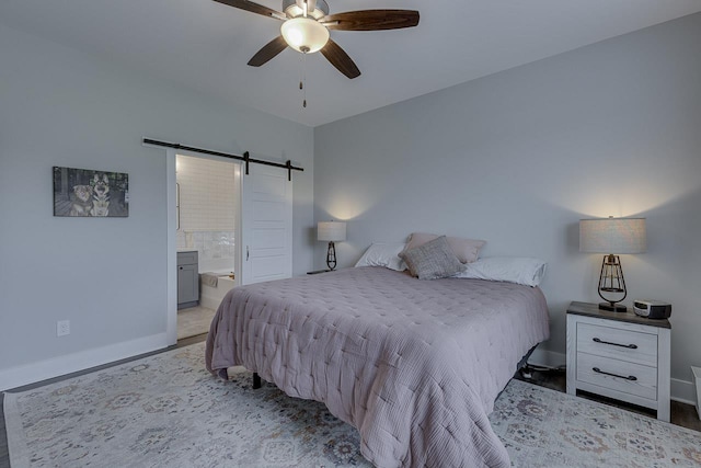 bedroom featuring a barn door, ensuite bathroom, light wood-style floors, and baseboards