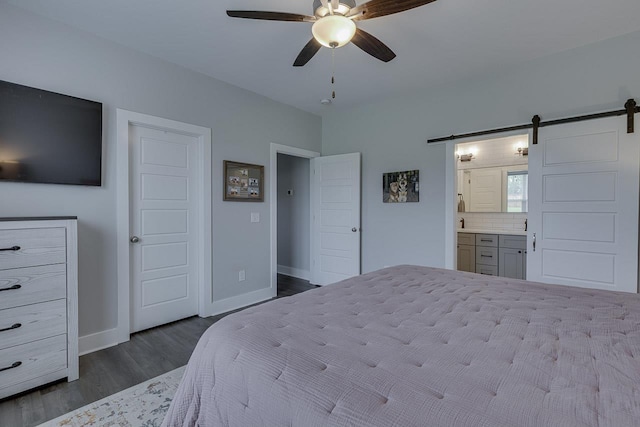 bedroom featuring connected bathroom, dark wood-style flooring, a barn door, and baseboards