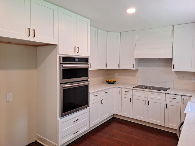 kitchen featuring double oven, white cabinetry, black electric stovetop, premium range hood, and dark wood finished floors