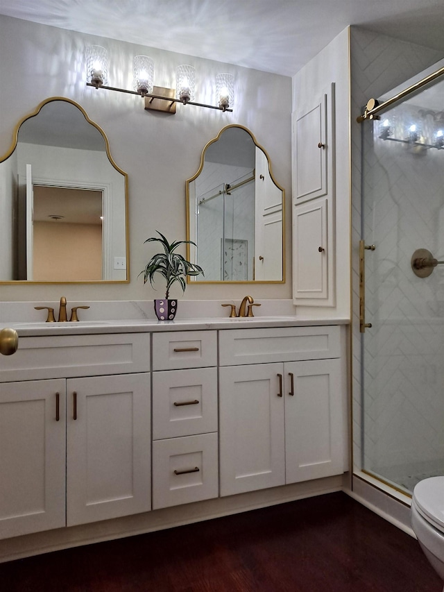 full bathroom with a sink, double vanity, a stall shower, toilet, and wood finished floors
