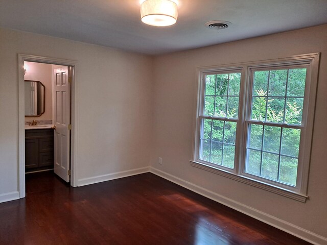 unfurnished room with dark wood-style floors, visible vents, a sink, and baseboards
