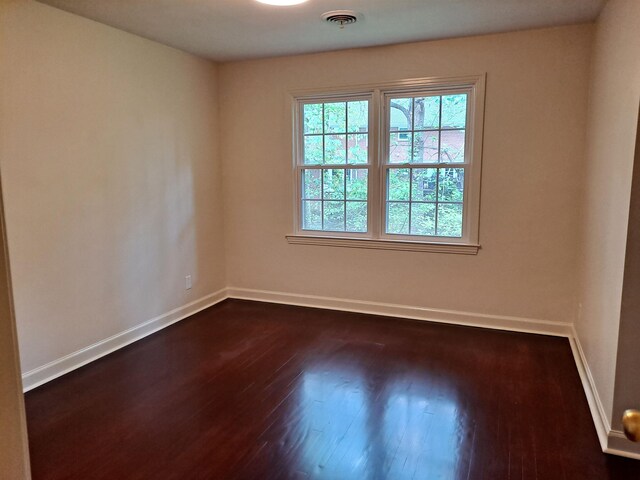 unfurnished room featuring dark wood-style floors, visible vents, and baseboards