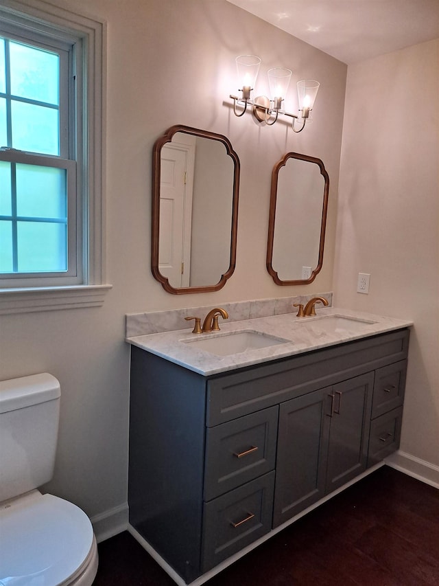 bathroom featuring baseboards, a healthy amount of sunlight, toilet, and a sink
