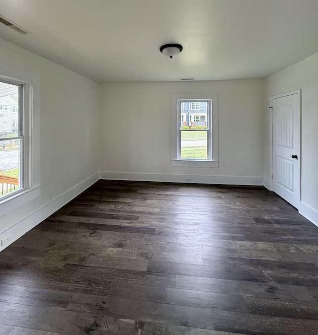 empty room with dark wood finished floors, visible vents, and baseboards