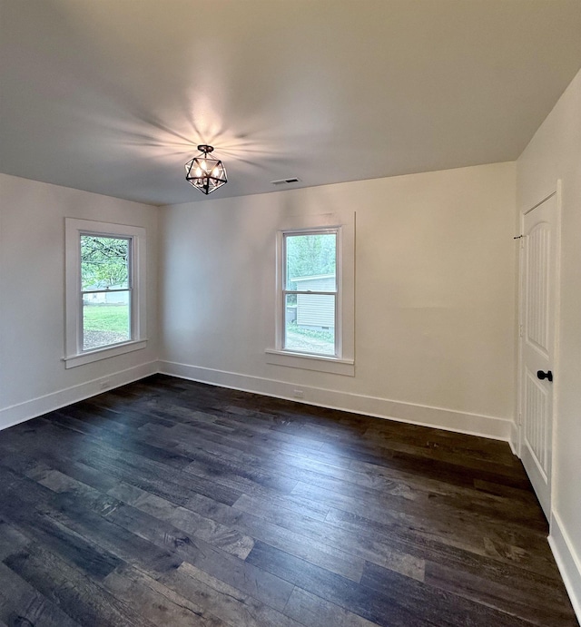 empty room with dark wood-style flooring, visible vents, and baseboards