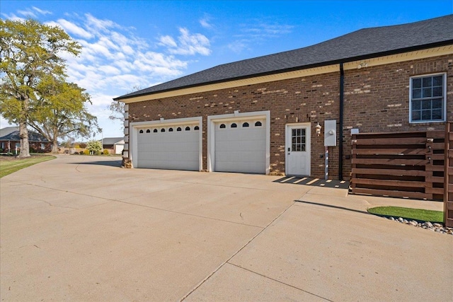 view of home's exterior with concrete driveway, a shingled roof, and brick siding