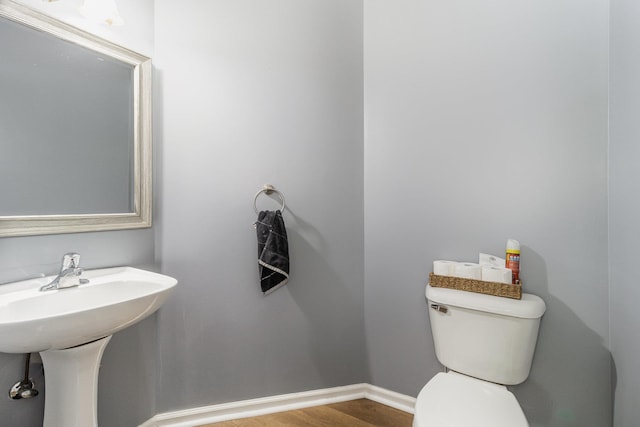 half bathroom with wood finished floors, toilet, and baseboards