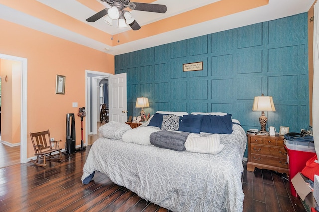 bedroom with an accent wall, a raised ceiling, dark wood-style floors, baseboards, and a towering ceiling
