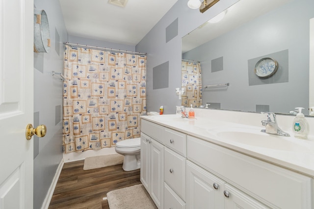 bathroom featuring toilet, double vanity, a sink, and wood finished floors