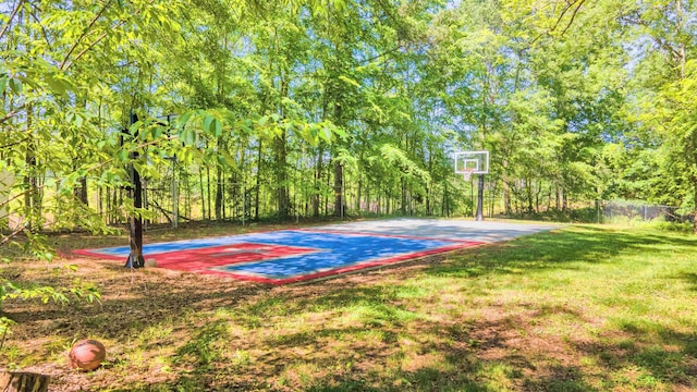 view of basketball court featuring fence, basketball hoop, and a lawn