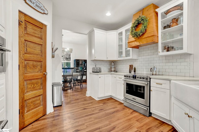 kitchen featuring electric stove, tasteful backsplash, light wood-style floors, custom range hood, and light countertops
