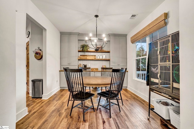 dining space featuring visible vents, light wood-type flooring, a notable chandelier, and baseboards