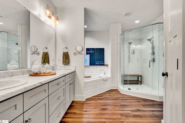 full bath with a sink, a stall shower, double vanity, a garden tub, and wood finished floors