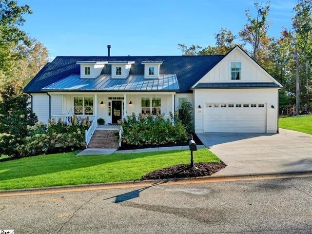 view of front of home featuring a standing seam roof, driveway, a front yard, and board and batten siding