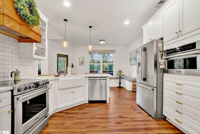 kitchen featuring custom range hood, visible vents, a peninsula, light countertops, and appliances with stainless steel finishes