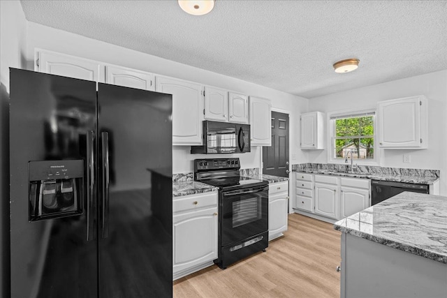 kitchen featuring a textured ceiling, white cabinets, a sink, black appliances, and light stone countertops