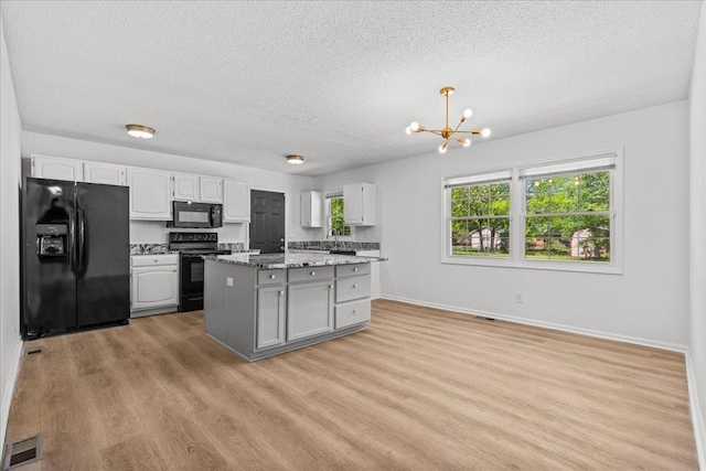 kitchen with an inviting chandelier, light wood-style flooring, a wealth of natural light, black appliances, and a textured ceiling