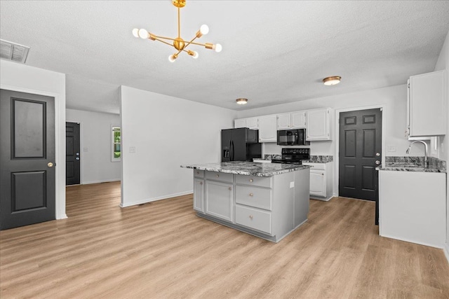 kitchen featuring an inviting chandelier, light wood-type flooring, black appliances, visible vents, and a kitchen island