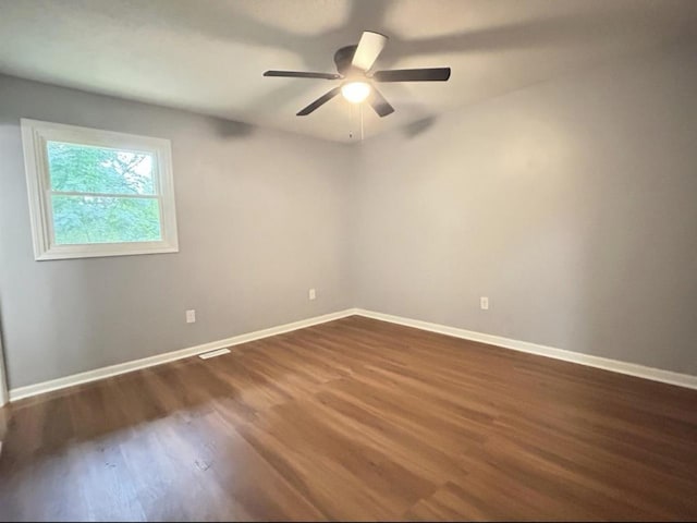 spare room featuring a ceiling fan, visible vents, baseboards, and dark wood-type flooring