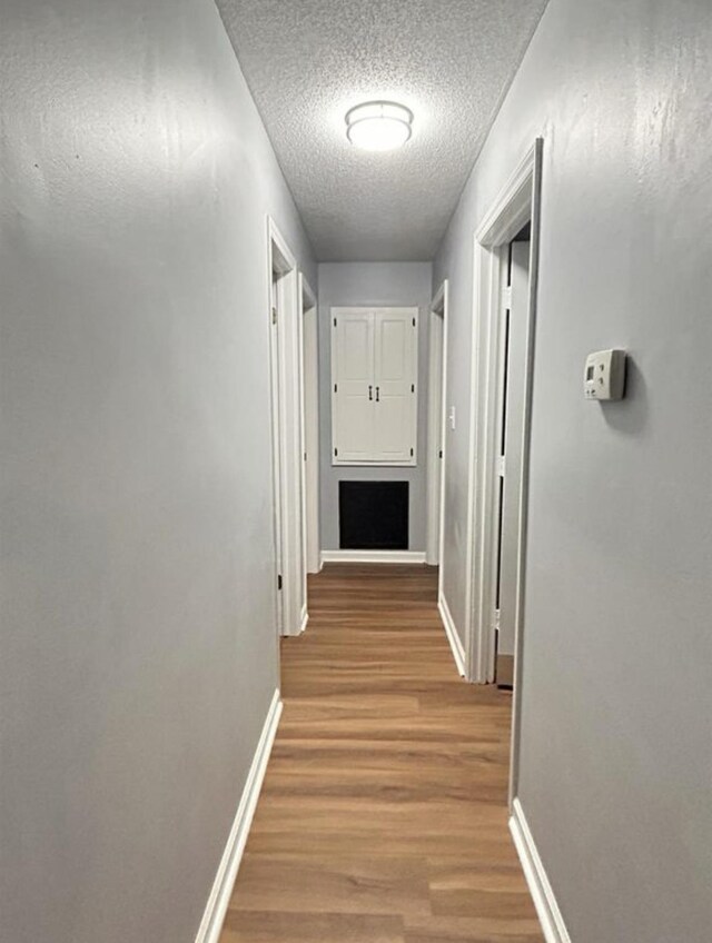corridor featuring a textured ceiling, wood finished floors, and baseboards